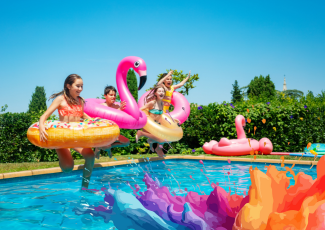 Kids jumping in pool on a sunny day outside with floaties and friends