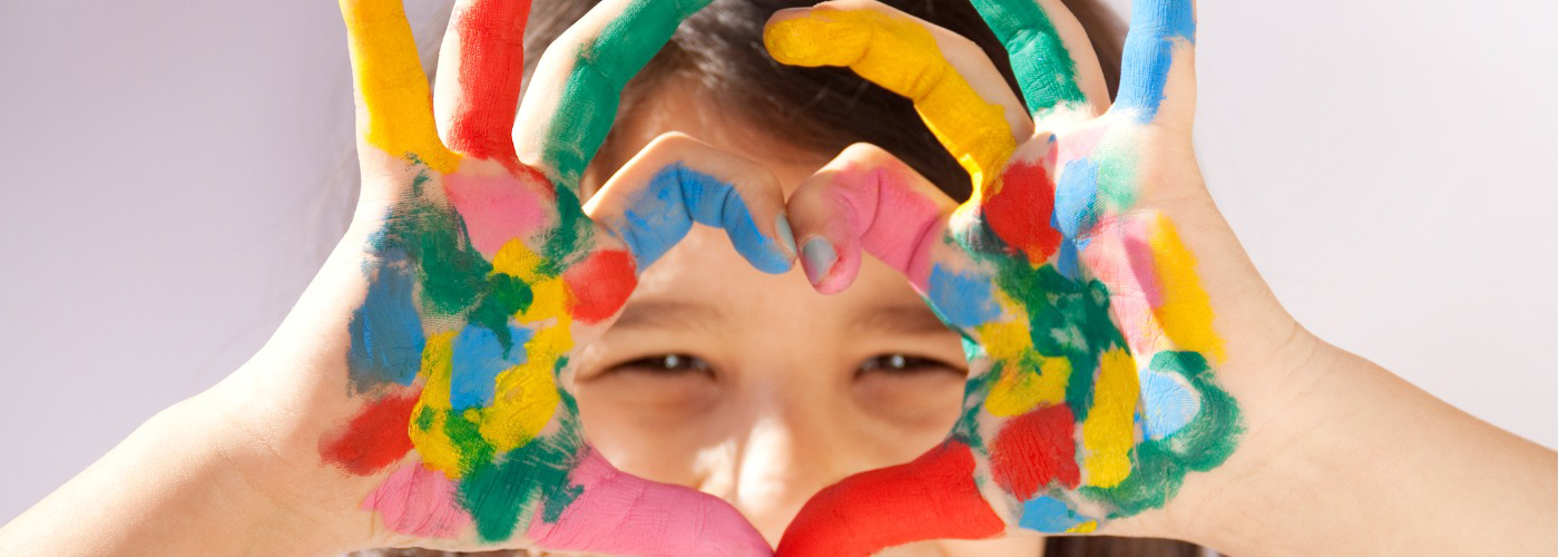 child with paint on hands in a heart shape.