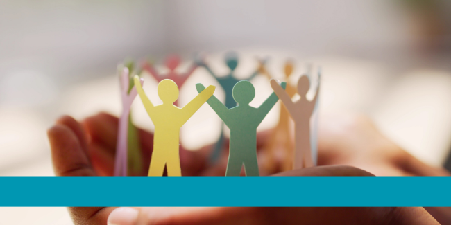 Hands holding paper cut out of people all holding raised hands in a circle, depicting community
