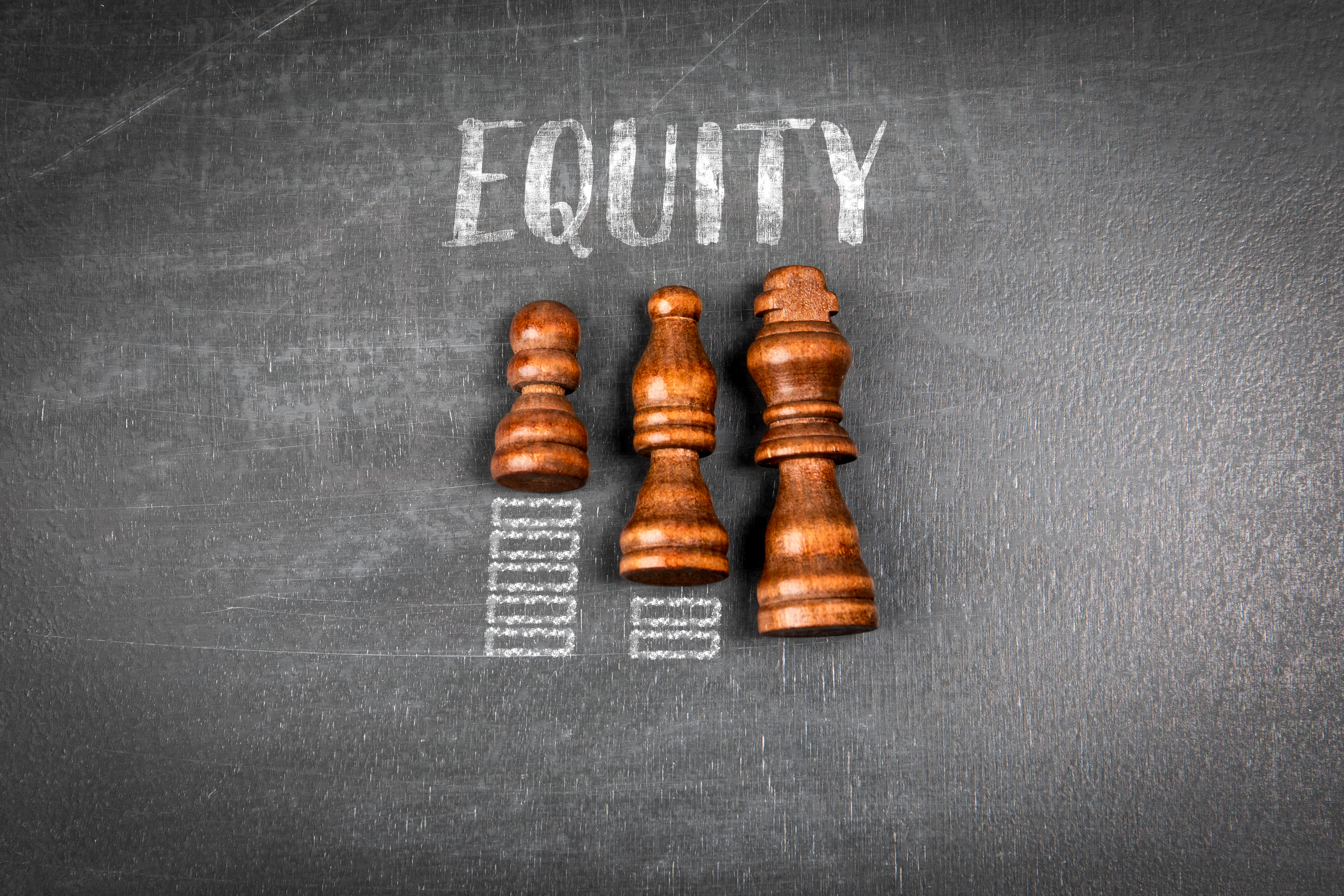Chalboard background with three chess pieces depicting equity