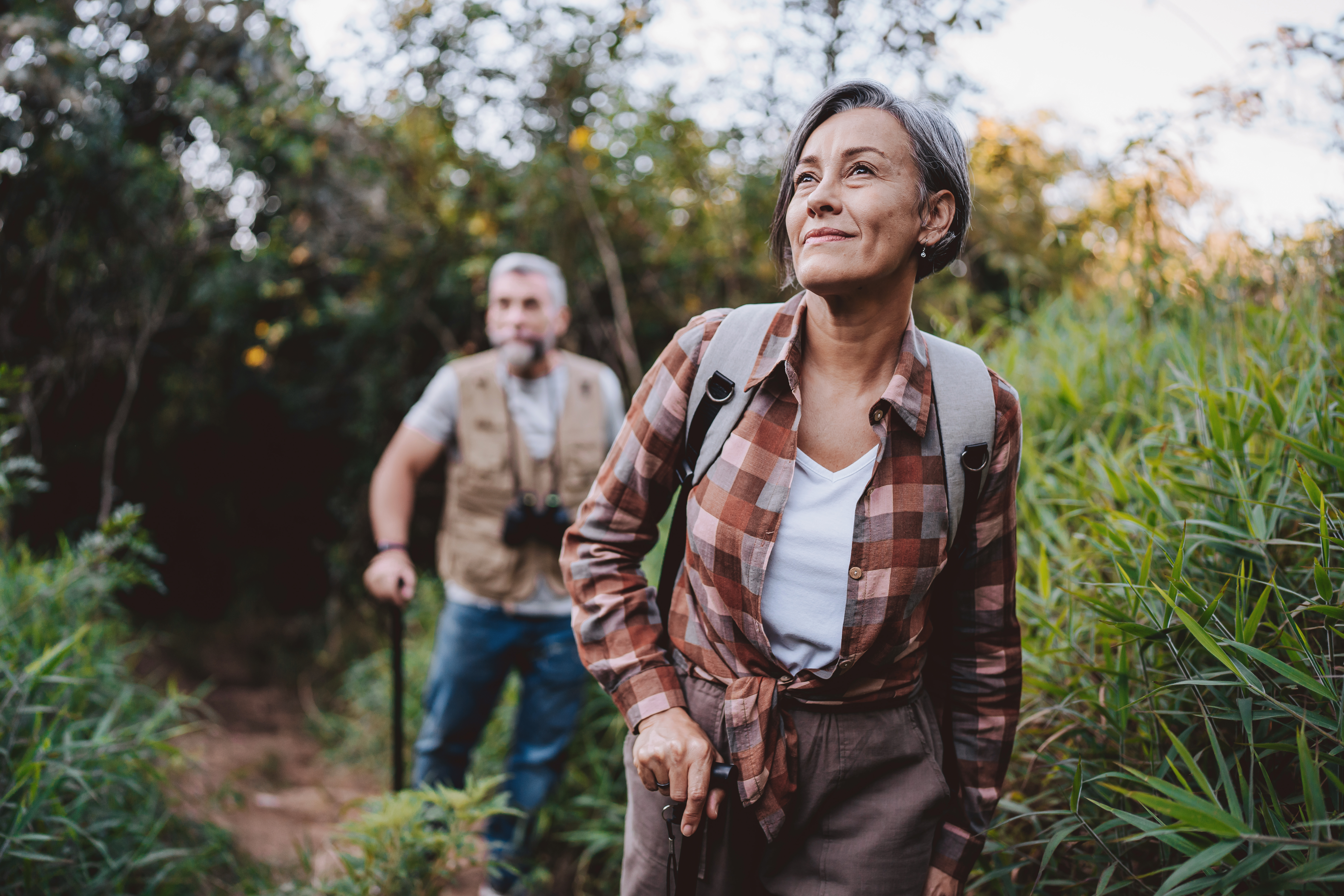 Woman in foreground, man blurred in background walking a trail with backpacks and walking sticks